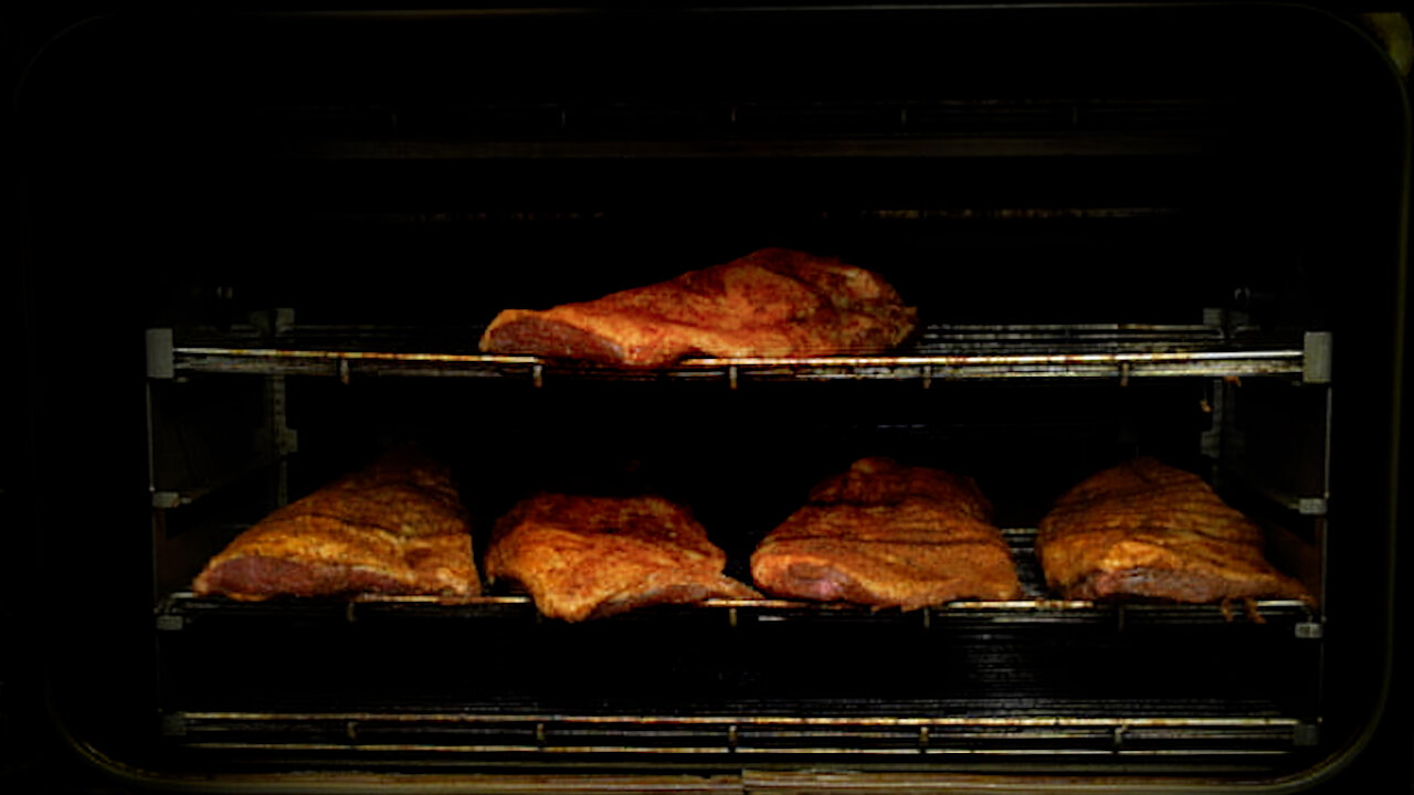 Briskets cooking inside a Southern Pride SP‑1400 rotisserie smoker, arranged on metal racks as they roast low and slow.